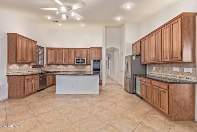 kitchen featuring arched walkways, brown cabinets, appliances with stainless steel finishes, a sink, and a kitchen island