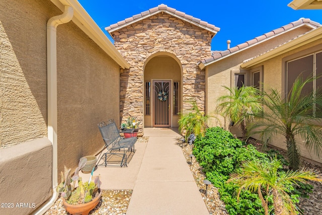 doorway to property featuring stone siding, a tiled roof, and stucco siding