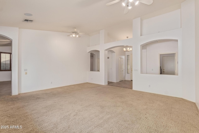 spare room featuring arched walkways, carpet flooring, and ceiling fan with notable chandelier