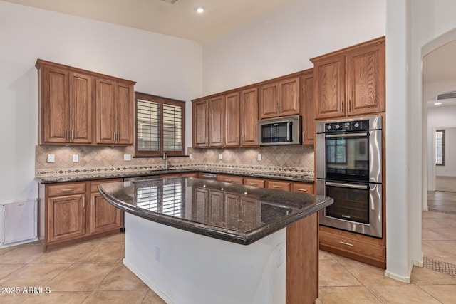 kitchen featuring brown cabinets, light tile patterned floors, stainless steel appliances, and a center island