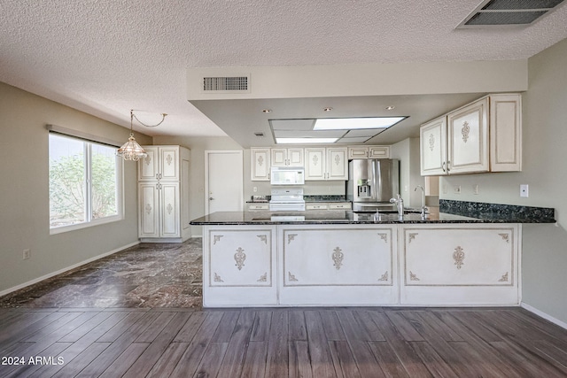 kitchen with dark hardwood / wood-style flooring, kitchen peninsula, dark stone counters, decorative light fixtures, and white appliances