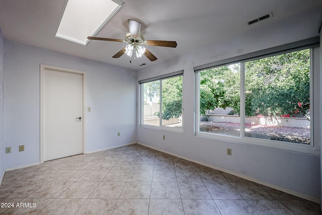 spare room featuring a skylight, ceiling fan, and light tile patterned floors