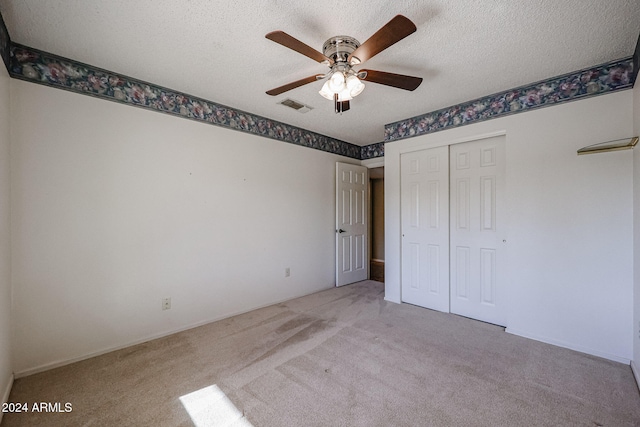 unfurnished bedroom featuring ceiling fan, light colored carpet, a textured ceiling, and a closet