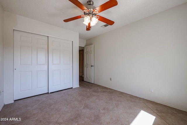 unfurnished bedroom with ceiling fan, a closet, light tile patterned flooring, and a textured ceiling