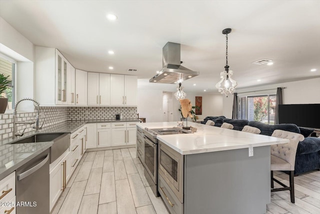 kitchen featuring island exhaust hood, a sink, light stone counters, open floor plan, and stainless steel appliances