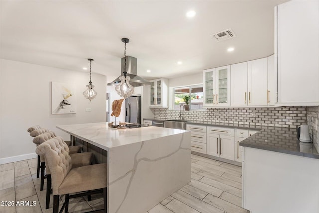 kitchen featuring stainless steel fridge, a sink, decorative backsplash, a kitchen island, and visible vents