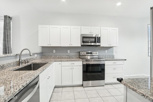 kitchen with light tile patterned floors, light stone countertops, white cabinetry, a sink, and stainless steel appliances