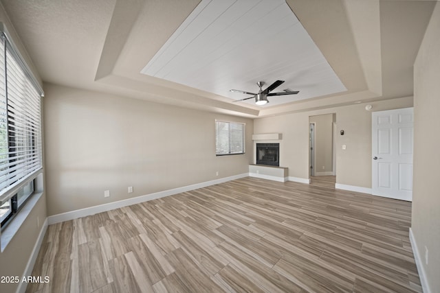 2105 W Terrace Dr, Wickenburg, AZ 85390 - unfurnished living room with light wood-style flooring, a ceiling fan, baseboards, a raised ceiling, and a fireplace with raised hearth