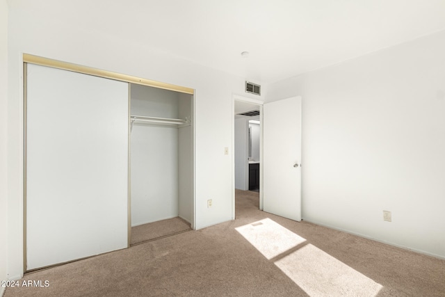 unfurnished bedroom with light colored carpet and a closet