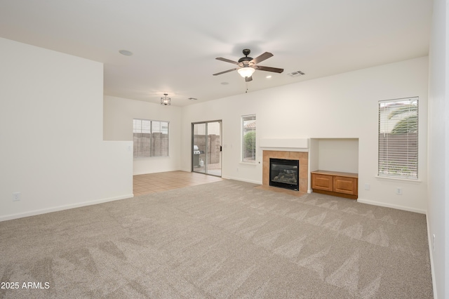 unfurnished living room with light colored carpet, a ceiling fan, baseboards, visible vents, and a tiled fireplace