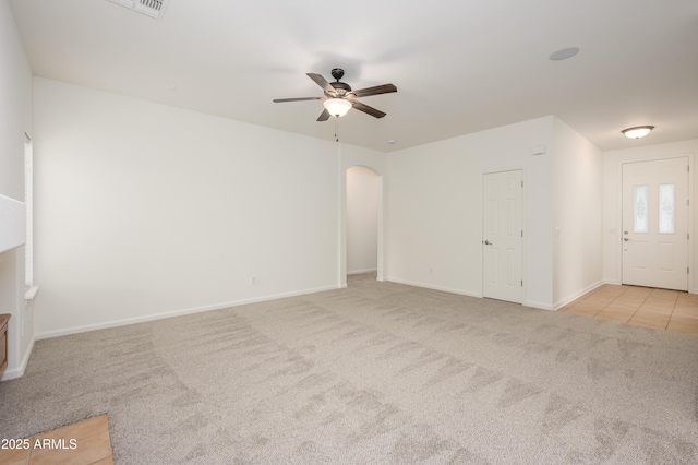 unfurnished living room with arched walkways, carpet flooring, a ceiling fan, and baseboards