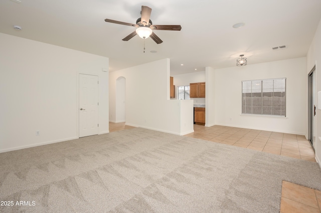 unfurnished living room with light tile patterned floors, visible vents, arched walkways, and light colored carpet