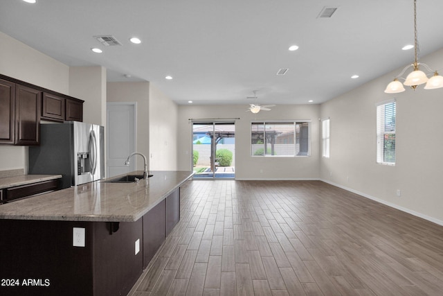 kitchen with stainless steel refrigerator with ice dispenser, hardwood / wood-style floors, sink, light stone counters, and a center island with sink