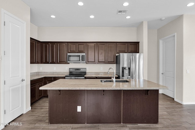 kitchen with sink, dark brown cabinetry, appliances with stainless steel finishes, and a center island with sink