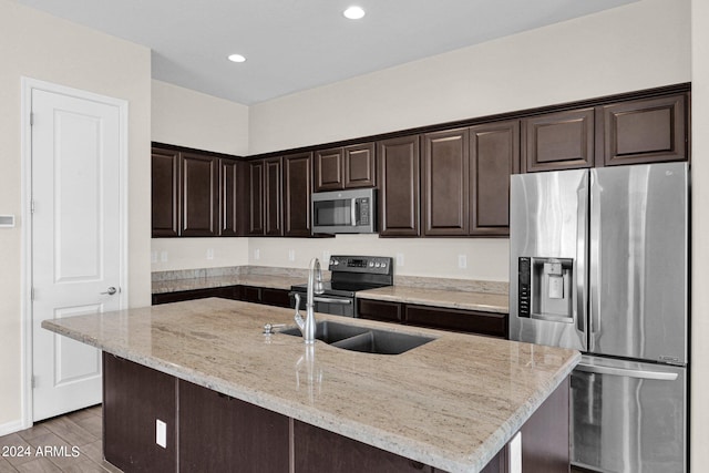 kitchen featuring light stone counters, a kitchen island, stainless steel appliances, dark brown cabinetry, and sink