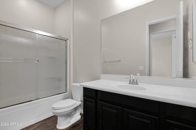 full bathroom featuring hardwood / wood-style floors, bath / shower combo with glass door, toilet, and vanity