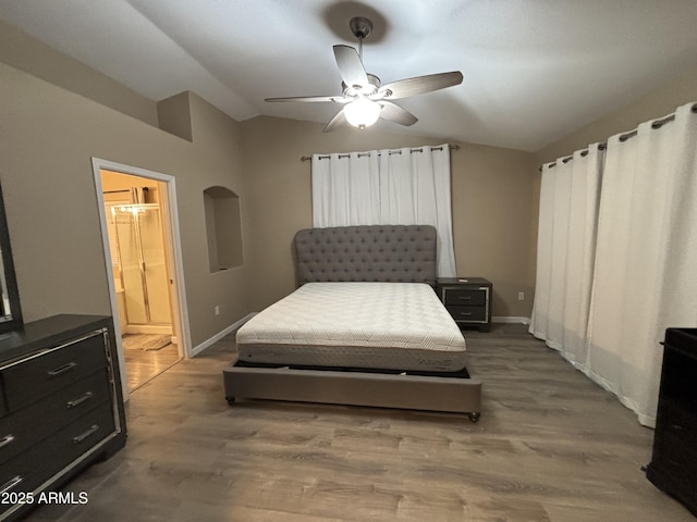 bedroom with a ceiling fan, wood finished floors, connected bathroom, baseboards, and vaulted ceiling