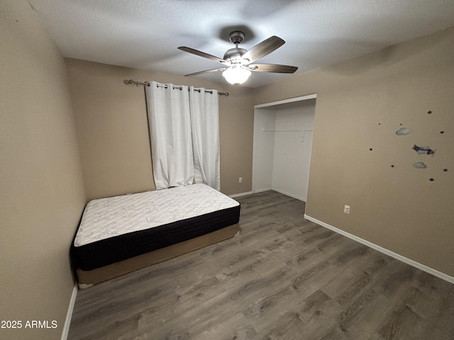 unfurnished bedroom featuring a ceiling fan, a textured ceiling, wood finished floors, a closet, and baseboards