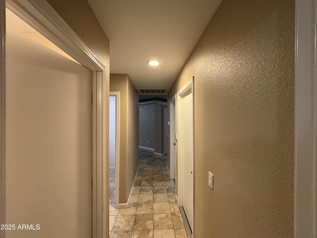 hallway featuring visible vents, baseboards, stone finish floor, and a textured wall