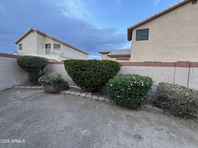 view of side of home with stucco siding, a tile roof, and fence