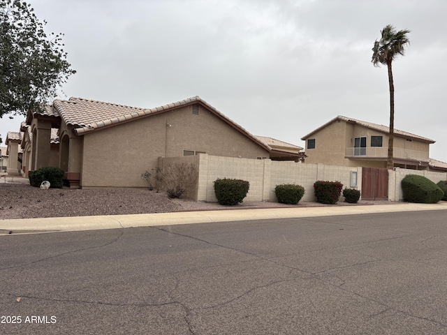 view of side of home with stucco siding, a tiled roof, and fence