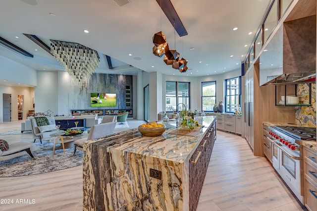 kitchen featuring range with two ovens, light hardwood / wood-style flooring, decorative light fixtures, light stone countertops, and an island with sink