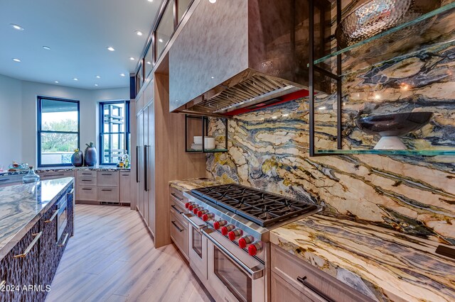 kitchen featuring range with two ovens, extractor fan, light wood-type flooring, tasteful backsplash, and light stone countertops