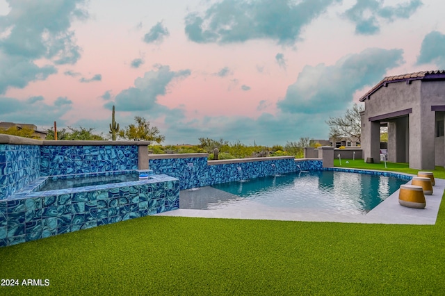 pool at dusk featuring a yard, a jacuzzi, and pool water feature