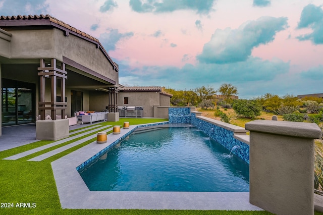 pool at dusk with a lawn, a patio area, and pool water feature