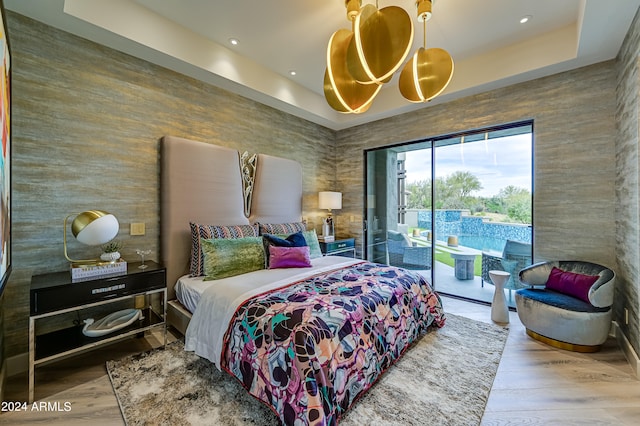 bedroom featuring access to exterior, hardwood / wood-style floors, and a tray ceiling