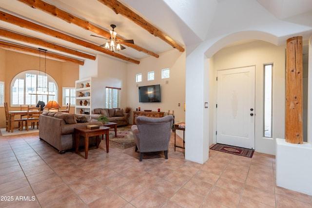 living area featuring a ceiling fan, beam ceiling, light tile patterned flooring, a healthy amount of sunlight, and arched walkways