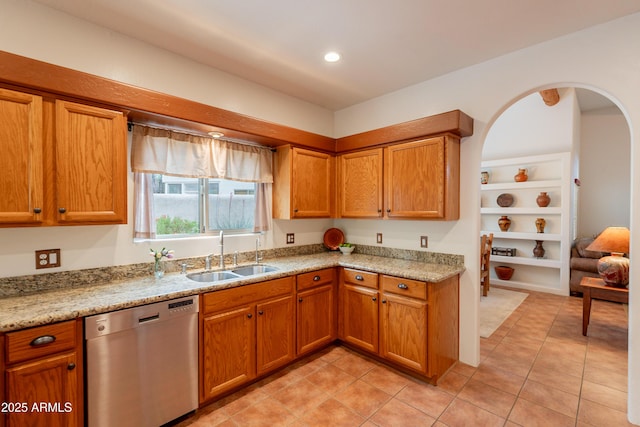 kitchen with stainless steel dishwasher, light tile patterned floors, brown cabinetry, and a sink