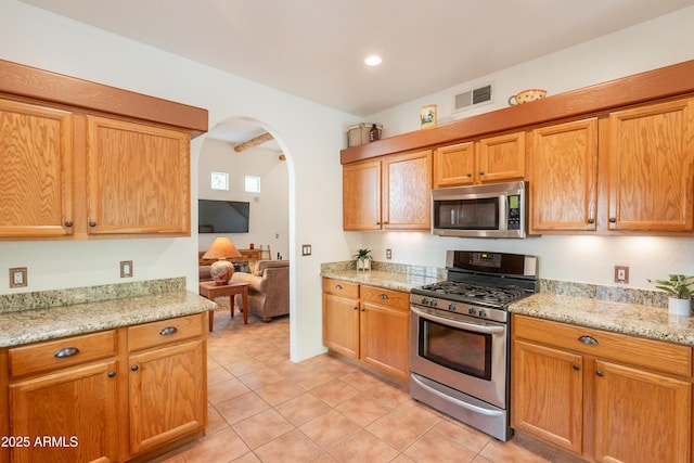 kitchen featuring light tile patterned flooring, appliances with stainless steel finishes, light stone counters, arched walkways, and visible vents