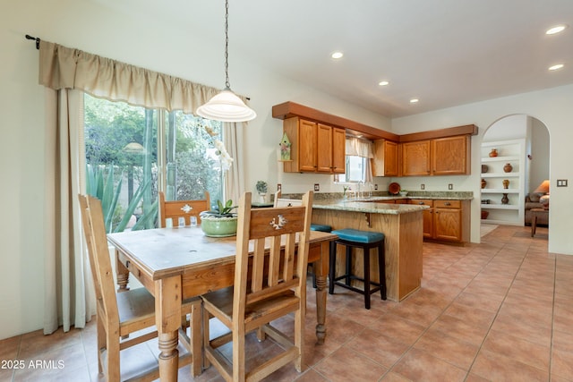 kitchen with recessed lighting, a peninsula, brown cabinets, and light stone countertops