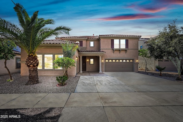 mediterranean / spanish-style home with a garage, driveway, a tiled roof, and stucco siding