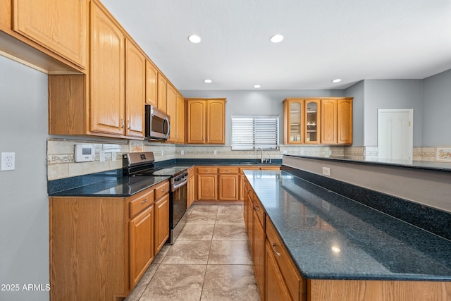 kitchen with tasteful backsplash, dark stone counters, glass insert cabinets, appliances with stainless steel finishes, and a sink