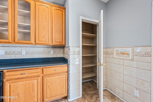 kitchen featuring light tile patterned floors, tile walls, wainscoting, dark countertops, and glass insert cabinets