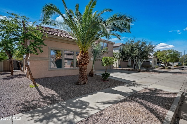 exterior space featuring a garage, fence, driveway, a tiled roof, and stucco siding