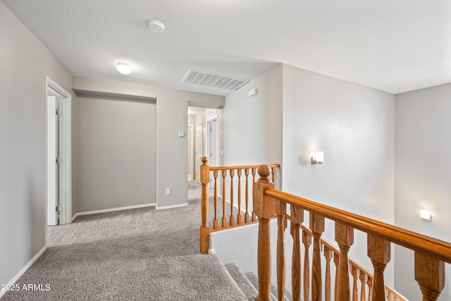 hall featuring carpet, an upstairs landing, visible vents, and baseboards