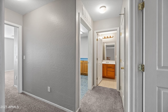 hallway with light colored carpet, a textured wall, and baseboards