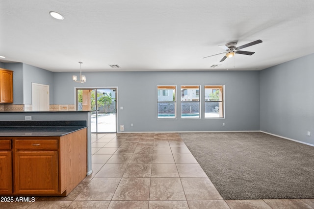 kitchen with ceiling fan with notable chandelier, light carpet, baseboards, open floor plan, and dark countertops