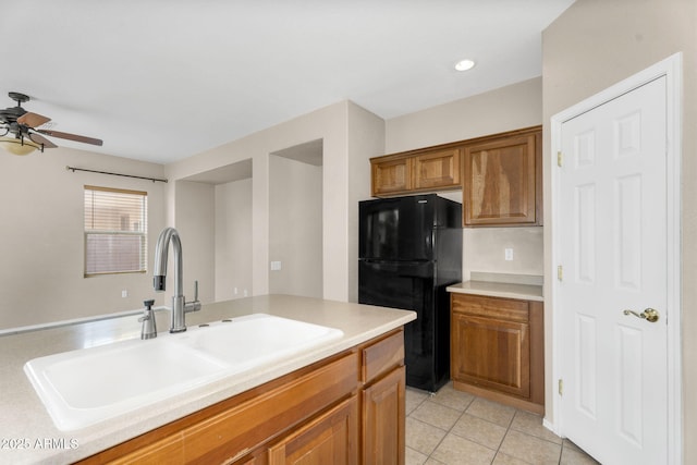 kitchen featuring a sink, freestanding refrigerator, brown cabinetry, light countertops, and light tile patterned floors