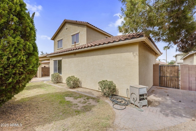 view of side of home featuring a tiled roof, stucco siding, a patio, and a gate