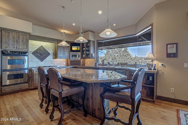 kitchen with decorative light fixtures, stainless steel appliances, light hardwood / wood-style flooring, and a kitchen island