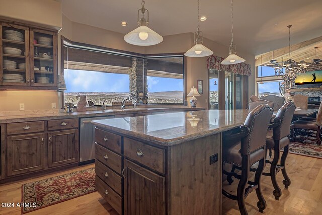 kitchen with dark stone countertops, pendant lighting, light hardwood / wood-style floors, a breakfast bar area, and dark brown cabinets