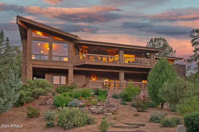 back house at dusk featuring a balcony and ceiling fan