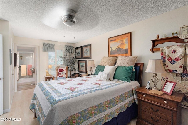 bedroom with ceiling fan, ensuite bath, light wood-type flooring, and a textured ceiling