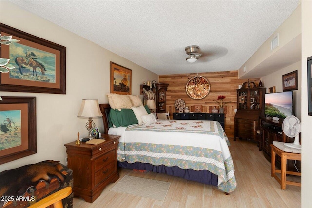 bedroom featuring a textured ceiling, ceiling fan, light hardwood / wood-style floors, and wooden walls