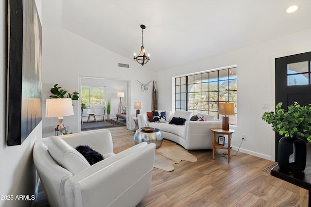 living room with vaulted ceiling, wood-type flooring, a healthy amount of sunlight, and a chandelier