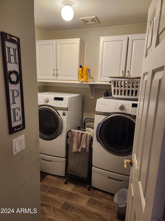 laundry room with washing machine and clothes dryer, dark wood-type flooring, and cabinets